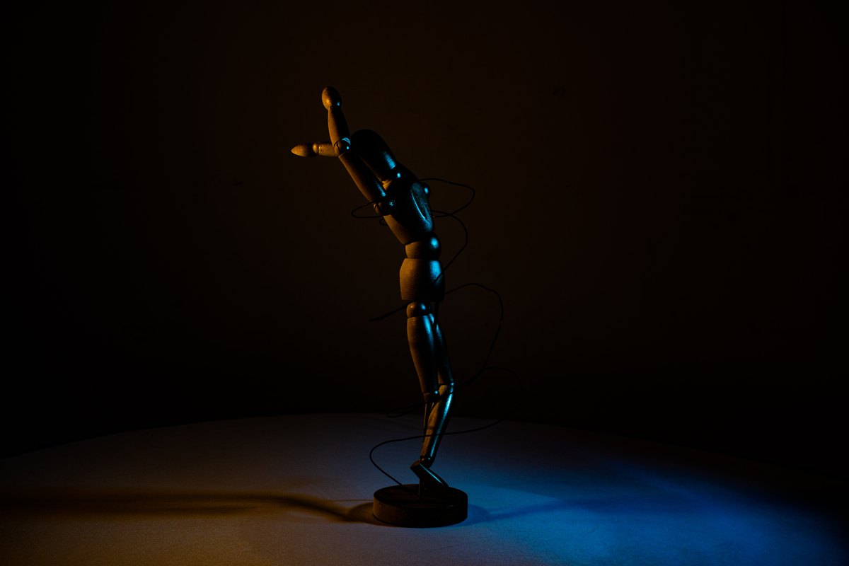 An articulated wooden figure lit in blue and amber against a dark background.