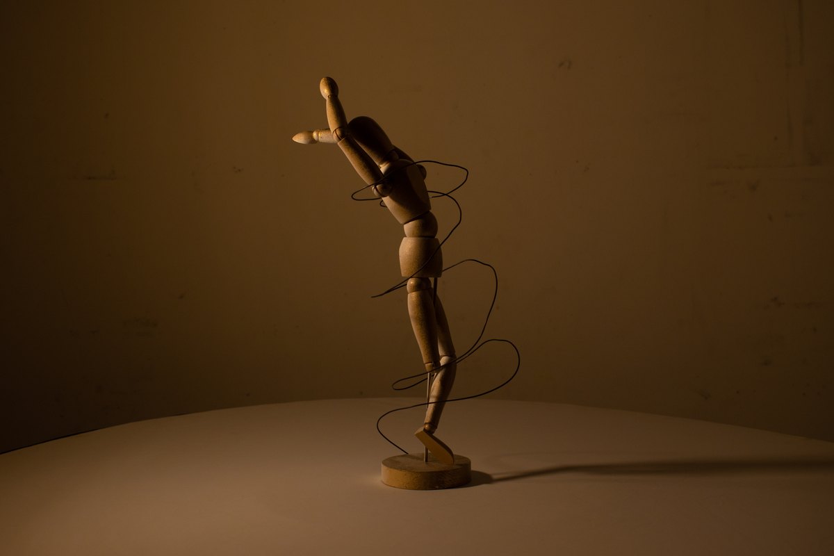 An articulated wooden figure and its shadow in warm light.