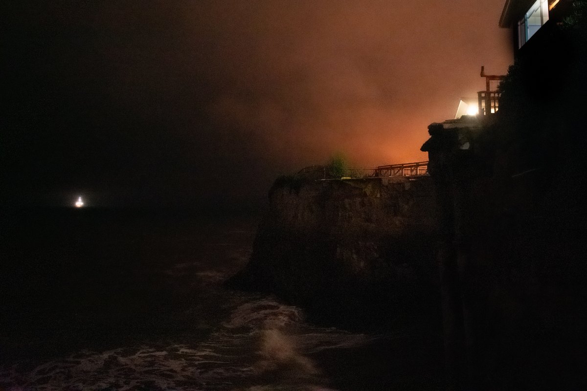Lights along the rocky shoreline of Del Playa shining through mist at night.