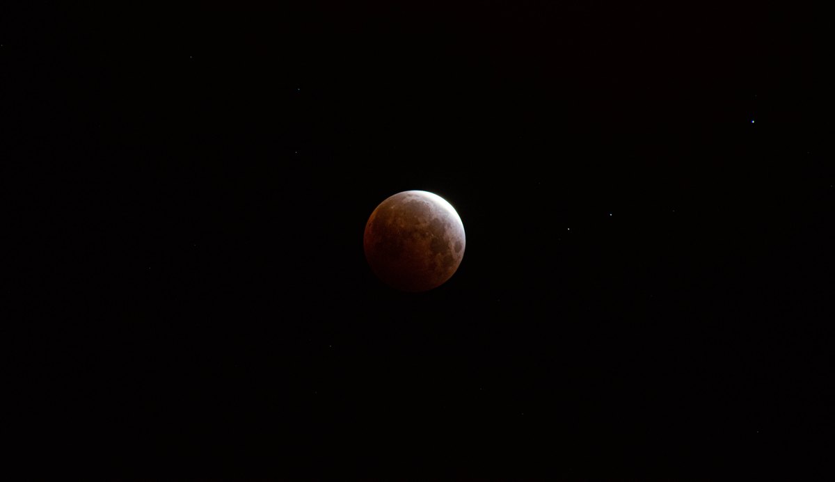 A reddish moon during a lunar eclipse, against a black sky.