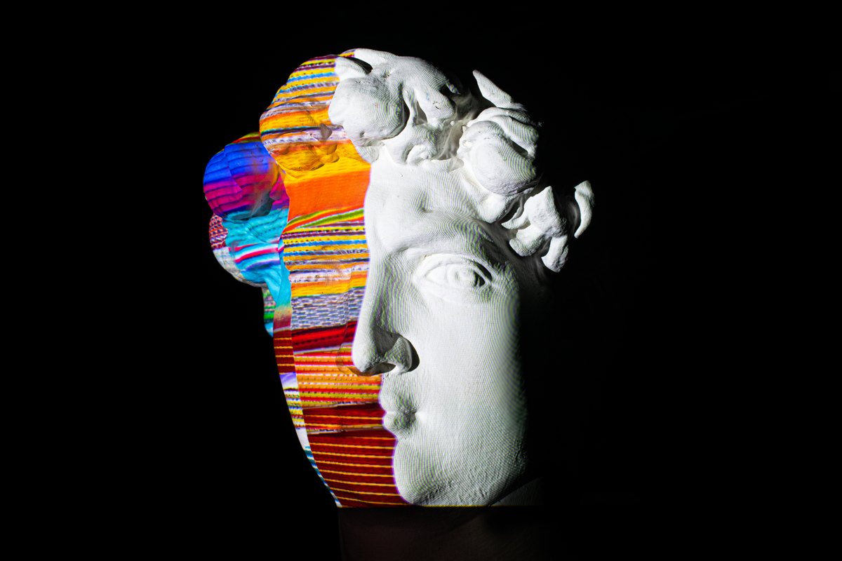 A sculpted face divided between white plaster and bright bands of color.